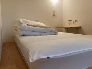 1 cama con sábanas blancas y almohadas en una habitación en HOSTEL HIROSAKI -Mixed dormitory-Vacation STAY 32012v en Hirosaki