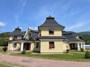 een groot geel huis met een zwart dak bij Penzión U dvoch levov in Oravský Podzámok