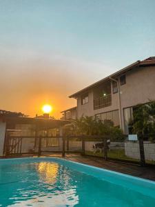 a house with a swimming pool in front of a sunset at Rosamar Suites in Praia do Rosa