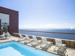 uma varanda com uma piscina com cadeiras e o oceano em Sol Victoria Marina Flat em Salvador