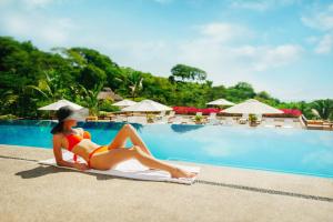 a woman in a bikini sitting on a towel next to a swimming pool at Grand Matlali Riviera Nayarit in Cruz de Huanacaxtle