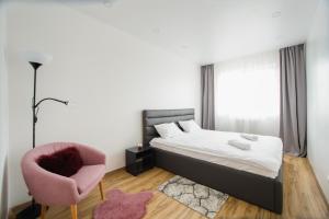 a bedroom with a bed and a pink chair at Elegant & Spacious – Central Apartment in Oradea