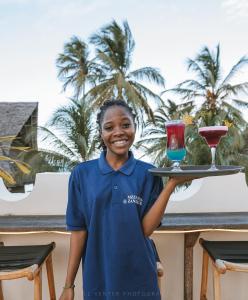 Eine Frau mit einem Tablett mit einem Glas Wein. in der Unterkunft Zanziblue in Matemwe