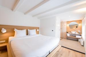 a bedroom with a large white bed and a bathroom at Zee van Tijd Holwerd in Holwerd