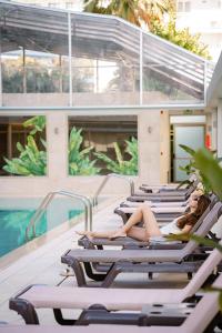 una mujer acostada en tumbonas junto a una piscina en Hotel Helios Lloret, en Lloret de Mar