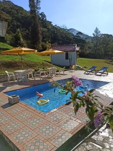 a swimming pool with chairs and a table and umbrella at Sitio Sao Jeronimo in Teresópolis