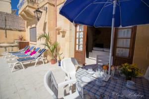 a patio with a table with a blue umbrella and chairs at Tal Lilly Xaghra in Xagħra