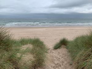 a sandy beach with some grass and the ocean at Brada View Bamburgh in Bamburgh