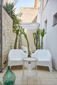 2 sedie bianche e un tavolo su un patio con cactus di Dimora Terranova Charming Rooms a Noto