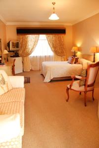 
a hotel room with a bed, chair, table and lamp at Fynbos Guest House Riversdale in Riversdale
