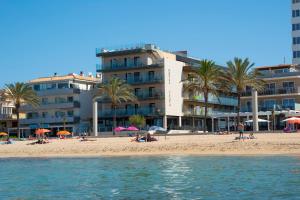 a beach with people sitting on the sand and a building at Hotel Playa Adults Only in Can Pastilla