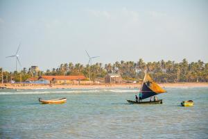 deux bateaux dans l'eau près d'une plage avec des moulins à vent dans l'établissement Parnaíba Hostel, à Parnaíba