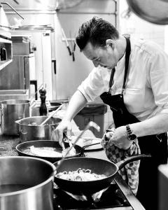 a man in a kitchen preparing food in a wok at Lebeau 19 Hotel in Knokke-Heist