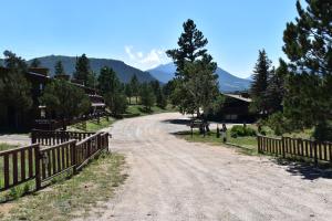 a dirt road with a fence and trees and mountains at Estes Lake Lodge in Estes Park