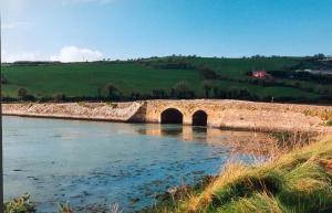 eine Steinbrücke über einen Fluss auf einem Feld in der Unterkunft Cottage by the Sea, West Cork, Ireland in Kilbrittain