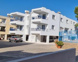 a large white building with cars parked in a parking lot at Latchi Area Apartments in Lachi