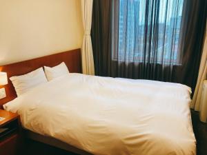 a white bed in a hotel room with a window at Dormy Inn Kanazawa Natural Hot Spring in Kanazawa