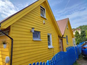 a yellow house with a blue fence in front of it at Piętrowe DOMKI KLIF 6os,Cudnie Bezludnie dzika plaża łąka bociek cisza szlaki rowerowe pieski 25zl in Debina