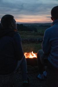 dos personas sentadas alrededor de una hoguera por la noche en Wild Northumberland Glamping en Hexham