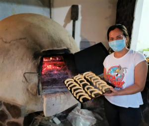 a woman in a mask holding a tray of food in an oven at YUMBILLA ECO LODGE in Cuispes