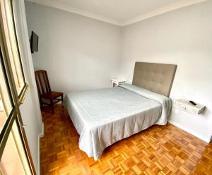 um quarto branco com uma cama e uma cadeira em Garden Lodge Hostal Evencio em Ribadavia