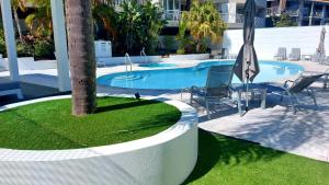 una piscina con una palmera, sillas y una sombrilla en Noosa Hill Resort, en Noosa Heads