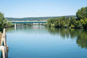 a view of a river with a bridge in the background at Paris Camping Ile du Roi in Triel-sur-Seine