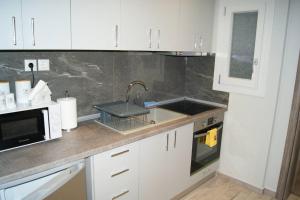 Una cocina con gabinetes blancos, un fregadero y un microondas. en Cozy City House, en Volos