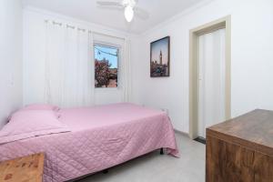 1 dormitorio con cama rosa y ventana en Aluguel Apartamento 2 quartos s/1 suíte | Bombas/SC, en Bombinhas