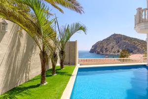 a pool with palm trees and the ocean in the background at Aparthotel Ola Blanca in Cala de Finestrat