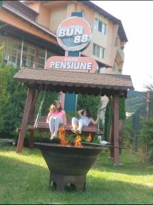 three girls sitting on a bench in front of a restaurant at Pensiunea Bun'88 in Corbeni