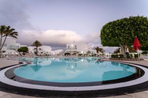 a large pool in a resort with palm trees and buildings at Hotel Lanzarote Village in Puerto del Carmen