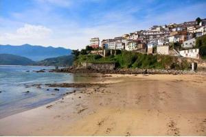 a sandy beach with houses on a hill next to the water at Pexe na mar in Lastres