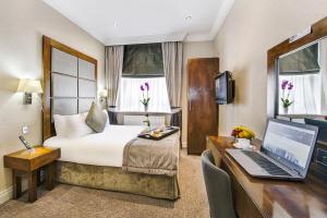 a hotel room with a bed and a desk with a laptop at Gem Langham Court Hotel in London