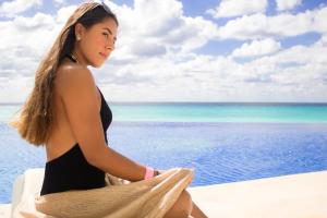 a woman in a black bikini sitting next to the ocean at Condominio Girasol OceanView in Cancún