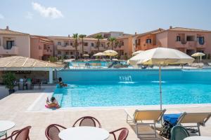 una piscina con mesas, sillas y edificios en Amareclub Red Sun Village, en Isola Rossa