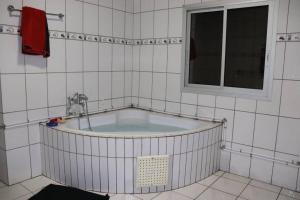 a bath tub in a white tiled bathroom with a window at Résidence Jeanne à Yaoundé Odza Messamengo in Yaoundé +49 photos