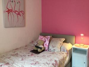 a teddy bear sitting on a bed with pink walls at Arun Sands Rooms in Littlehampton