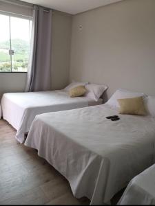 2 Betten in einem weißen Zimmer mit Fenster in der Unterkunft Cantinho da Alegria Suítes in Capitólio