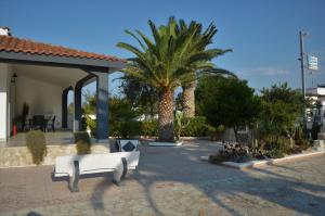 a white bench in a courtyard with palm trees at B&B Poseidon in Punta Prosciutto