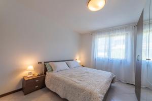 a white bedroom with a bed and a window at La Feriolina - Appartamento al lago con giardino privato in Baveno