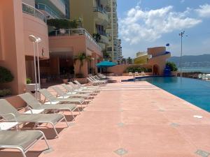 a row of lounge chairs next to a swimming pool at Comfortable Beachfront apartment in Acapulco in Acapulco