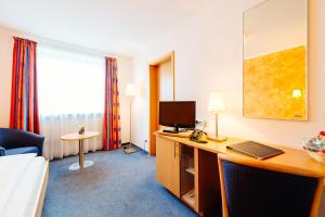 Habitación de hotel con cama y escritorio con TV. en Hotel Graf Lehndorff zur Messe, en Múnich