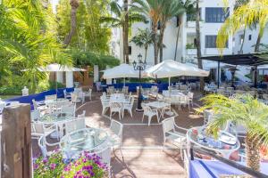 a patio with white tables and chairs and palm trees at Jardines de las Golondrinas in Marbella