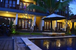 an umbrella and benches next to a pool in front of a building at Dabumito Guest House in Canggu