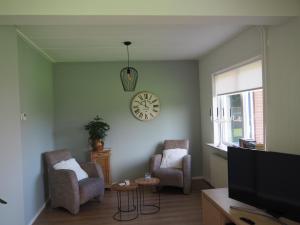 een woonkamer met 2 stoelen en een klok aan de muur bij Reggezicht; Mooi huis op een prachtige plek! in Hellendoorn