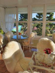 - un salon avec des chaises blanches, une table et des fenêtres dans l'établissement Pousada Chateau Colinas, à Campos do Jordão