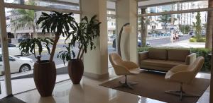 a lobby with two chairs and a couch and palm trees at Em Capao da Canoa - Luxo e conforto com praia , sol e mar em Capão. in Capão da Canoa