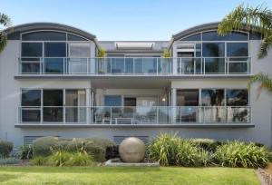 a large white house with a large balcony at Modern Beach Apartment with Pool & Location in Mount Maunganui