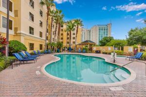 a swimming pool with chairs and palm trees and buildings at 1BR with King Bed - Near Disney - Pool and Hot Tub! in Orlando